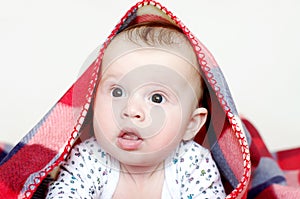 Surprised baby age of 4 months covered by checkered plaid