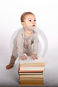 Surprised baby boy in cream clothes playing with books