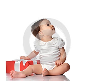 Surprised baby in jumpsuit sitting with gift box looking aside