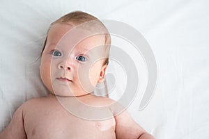 The surprised baby lies on a white blanket. The concept of interest