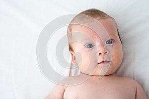 The surprised baby lies on a white blanket. The concept of interest