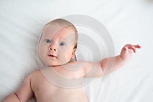 The surprised baby lies on a white blanket. The concept of interest