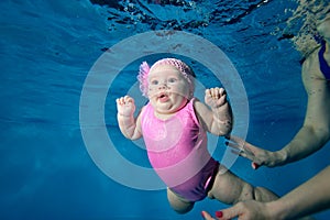 Surprised baby under the water in a red swimsuit on a blue background surrounded by bubbles. A little girl with blue