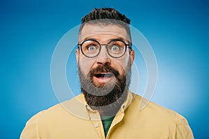 Surprised bearded man in eyeglasses looking at camera isolated