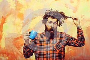 Surprised bearded man pulling stylish fringe hair with blue cup