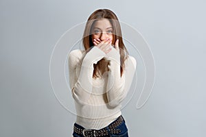 Surprised beautiful girl covers her mouth with her hands and looks at the camera.