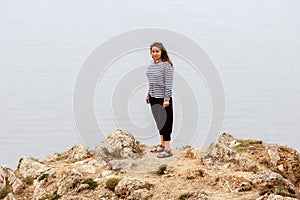 A surprised beautiful girl stands on a rock above the water