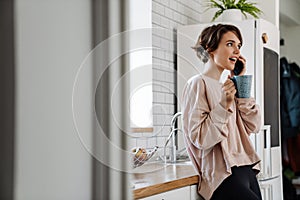 Surprised beautiful girl talking on cellphone while drinking coffee