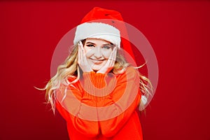 a surprised beautiful woman in a Santa Claus hat on a red background.