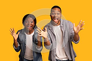 Surprised Black Couple Exclaiming With Excitement And Spreading Hands Over Yellow Background