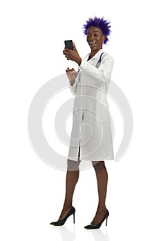 Surprised black female doctor is standing with telephone and laughing. Front view, full length, isolated