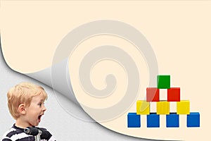 Surprised blond boy is looking at a pyramid of wooden toy
