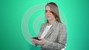 Surprised blonde girl texting on mobile phone while standing isolated over green background