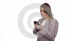 Surprised blonde girl texting on mobile phone while standing isolated over white background