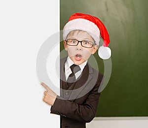 Surprised boy in Santa red hat looks out from behind a banner