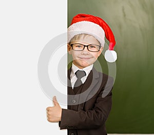 Surprised boy in Santa red hat looks out from behind a banner and showing thumbs up