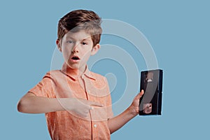 Surprised boy showing video cassette on blue background