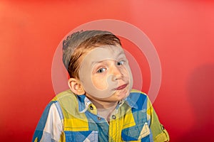 The surprised boy shrugs and does not know what to do, on a red background