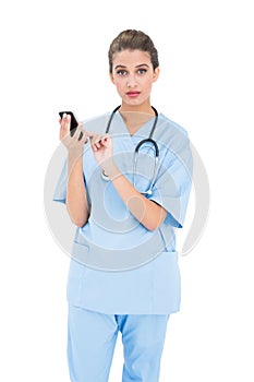 Surprised brown haired nurse in blue scrubs using a mobile phone