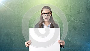 Surprised Business woman portrait with blank white board on green isolated . Female model with long hair in glasses.