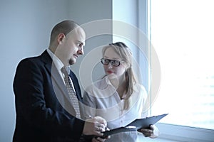 Surprised businessman and assistant discussing business documents standing near office window