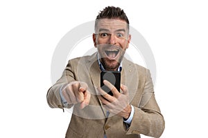 Surprised businessman with beard holding phone and pointing finger