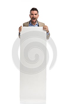 Surprised businessman in suit hiding his body behind empty board