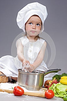 Surprised Caucasian Little Girl In Cook Uniform With Saucepan In Studio