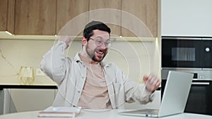 Surprised caucasian man looking at screen of laptop and making winner gesture