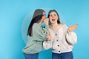 A surprised caucasian woman listens to her twin sister secret. Amazement on blue background