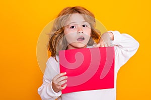 Surprised child boy showing empty sheet of paper, isolated on yellow background. Portrait of a kid holding a blank