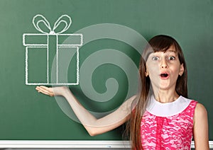 Surprised child girl hold drawn gift box near school blackboard