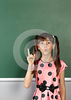 surprised child girl show with a finger empty school blackboard, copy space