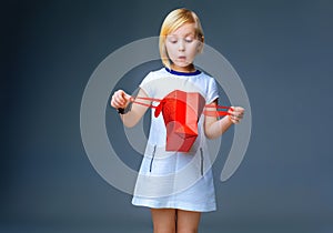 Surprised child on grey looking in red christmas shopping bag