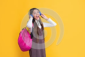 surprised child in headphones with school backpack on yellow background