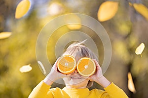 Surprised child holding slices of orange in autumn park