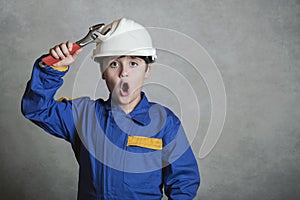 Surprised child with a white helmet and holding a wrench