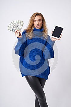Surprised curly blond woman with tablet and money in hand