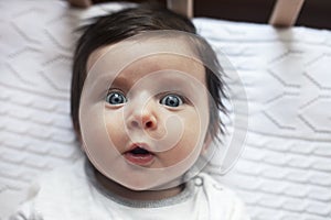 Surprised cute baby with blues eyes close portrait, lying in bed