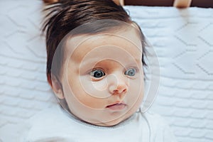 Surprised cute baby with blues eyes close portrait, lying in bed