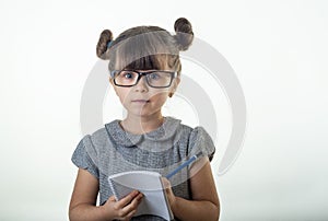Surprised cute child in eyeglasses, writing in notebook using pencil, keeping mouth wide open.