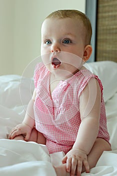 Surprised cute little Caucasian baby sits on the bed.