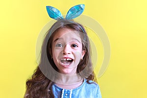 Surprised cute little child girl wearing bunny ears on yellow background. Happy Easter! Spring greeting card with copy space