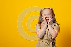 Surprised cute little girl child isolated over yellow background.  Hands near open mouth looking at camera. Copy space