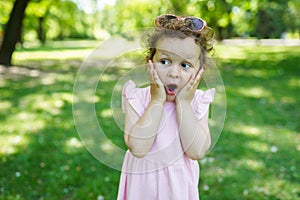 Surprised cute little toddler girl child in pink dress on nature background. Advertising childrens products
