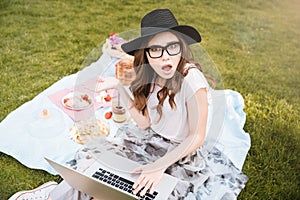 Surprised cute young woman using laptop on picnic