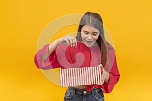 Surprised and delighted girl looks into an open gift box. Portrait of young brunette girl with gift in her hands