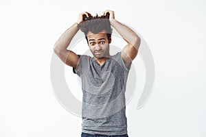 Surprised displeased african man looking down touching hair. White background.