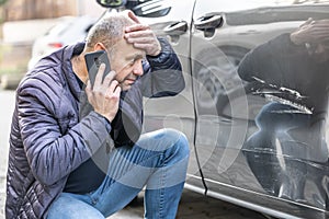 A surprised driver calls the insurance company or the police because an unknown culprit has damaged his car photo