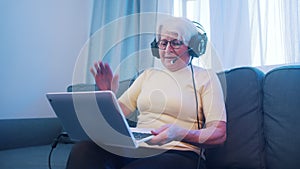 Surprised elderly woman with headset waving to laptop camera. Lockdown and entertainment